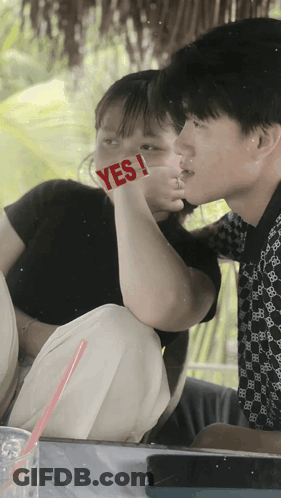 A Boy And A Girl Are Kissing With The Girl Holding A Sign That Says Yes GIF