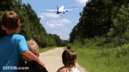 A Boy And A Girl Are Looking At An Airplane Flying Over Them GIF