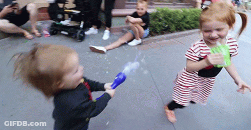 A Boy And A Girl Are Playing With Bubbles On The Sidewalk . GIF