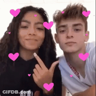 A Boy And A Girl Are Posing For A Picture With Pink Hearts Around Them . GIF