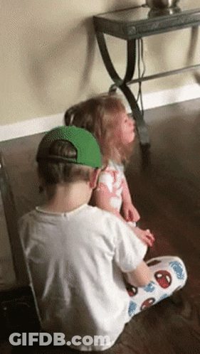 A Boy And A Girl Are Sitting On A Wooden Floor GIF