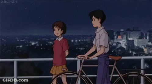 A Boy And A Girl Are Standing Next To A Bicycle On A Balcony Overlooking A City At Night . GIF