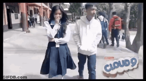 A Boy And A Girl Are Standing Next To Each Other On A Sidewalk . The Girl Is Covering Her Mouth . GIF