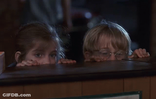 A Boy And A Girl Peeking Over A Counter In A Dark Room GIF