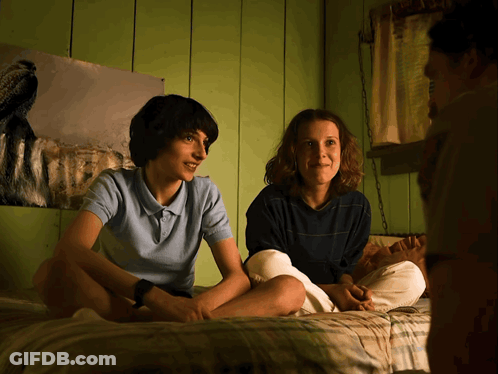 A Boy And A Girl Sit On A Bed In Front Of A Painting Of A Dog GIF