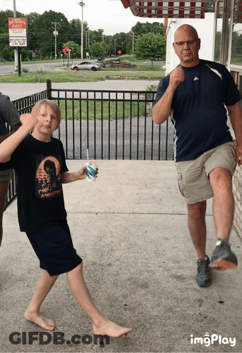 A Boy Holding A Cup Of Ice Cream Stands Next To Two Men GIF