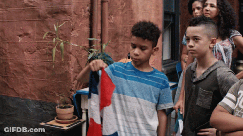 A Boy In A Blue And White Shirt Is Holding A Red White And Blue Flag GIF