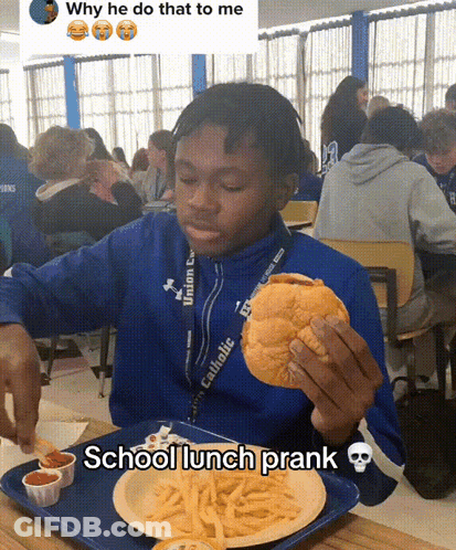 A Boy In A Blue Jacket Is Eating A Hamburger And French Fries At A School Lunch GIF