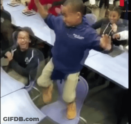 A Boy In A Blue Shirt Is Jumping In The Air While Sitting On A Chair In A Classroom . GIF