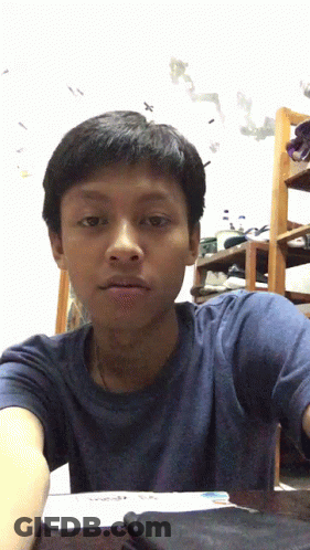 A Boy In A Blue Shirt Is Sitting At A Desk GIF