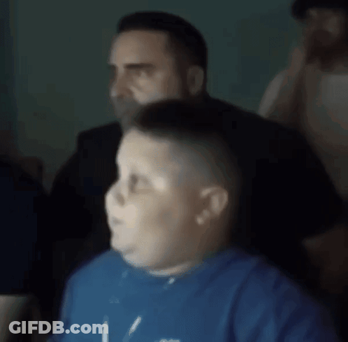 A Boy In A Blue Shirt Is Sitting In Front Of A Man In A Black Shirt GIF
