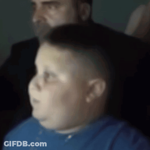 A Boy In A Blue Shirt Is Sitting In Front Of A Man In A Suit GIF