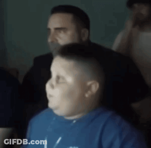 A Boy In A Blue Shirt Is Sitting In Front Of A Man . GIF