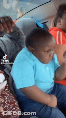 A Boy In A Blue Shirt Is Sitting In The Back Seat Of A Car With A Tik Tok Watermark GIF