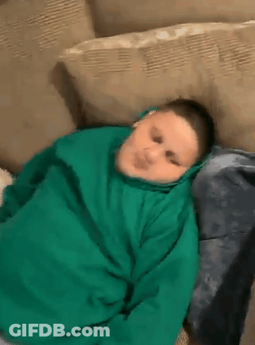 A Boy In A Green Hoodie Is Laying On A Couch . GIF