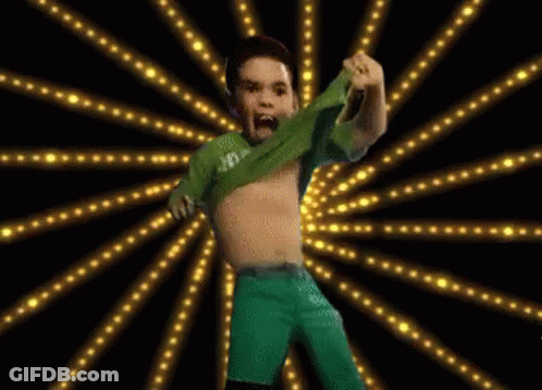 A Boy In A Green Shirt And Green Shorts Is Dancing In Front Of A Burst Of Lights GIF