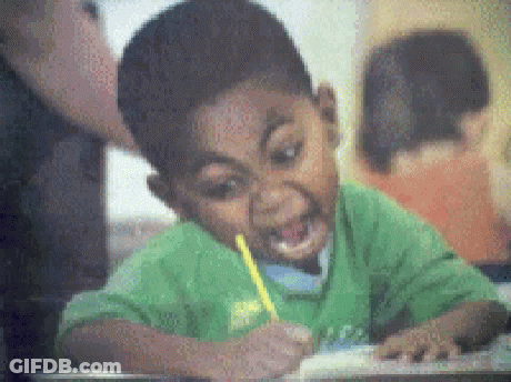 A Boy In A Green Shirt Is Writing On A Piece Of Paper With A Pencil In His Mouth . GIF