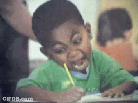 A Boy In A Green Shirt Is Writing With A Yellow Pencil In His Mouth . GIF