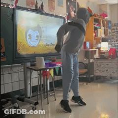 A Boy In A Hoodie Is Dancing In Front Of A Large Screen With A Face On It GIF
