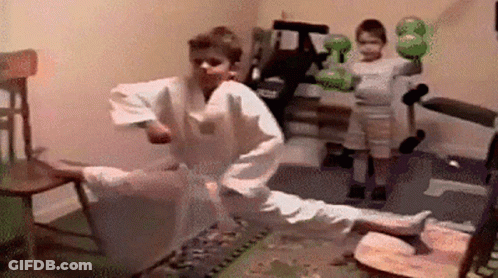 A Boy In A Karate Uniform Is Kicking A Chair While Another Boy Holds A Boxing Glove . GIF