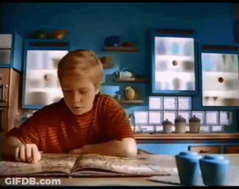 A Boy In A Red Shirt Is Reading A Book In A Kitchen GIF