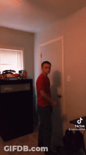 A Boy In A Red Shirt Is Standing In Front Of A Door In A Room GIF