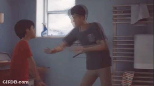 A Boy In A Red Shirt Is Standing Next To Another Boy In A Room GIF