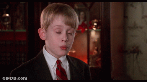 A Boy In A Suit And Tie Is Blowing A Kiss In Front Of A Bookcase GIF