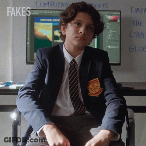 A Boy In A Suit And Tie Is Sitting In Front Of A Computer Screen With Fakes Written On The Wall Behind Him GIF