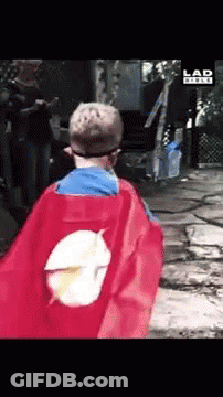 A Boy In A Superhero Cape Is Walking In Front Of A Sign That Says Lad GIF