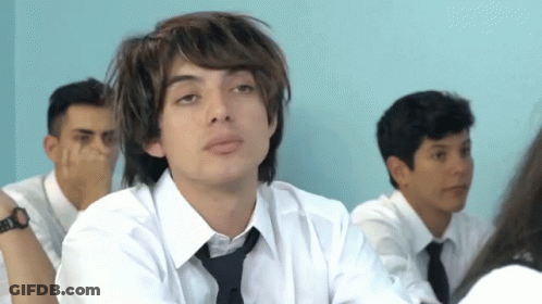 A Boy In A White Shirt And Tie Is Sitting In A Classroom GIF