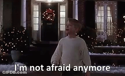 A Boy In A White Sweater Is Standing In Front Of A House With Christmas Lights On It . GIF