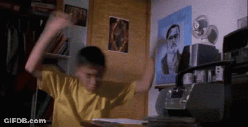 A Boy In A Yellow Shirt Is Dancing In A Room With A Picture Of A Man On The Wall Behind Him GIF