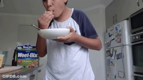 A Boy Is Eating Weet-Bix Cereal From A Bowl GIF
