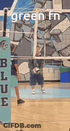 A Boy Is Holding A Volleyball In Front Of A Volleyball Net With The Words Green Fn On It . GIF