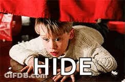 A Boy Is Laying On The Floor Under A Red Curtain With The Words `` Hide '' Written On It . GIF