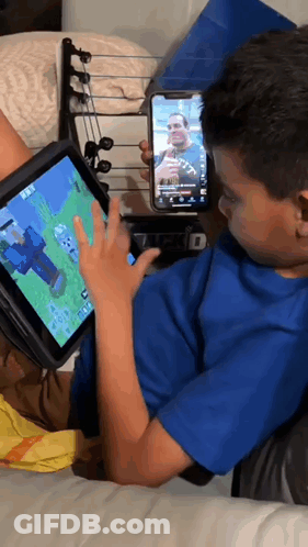 A Boy Is Playing A Video Game On A Tablet While Another Boy Holds A Cell Phone GIF