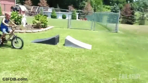 A Boy Is Riding A Bike Down A Ramp In A Grassy Field . GIF