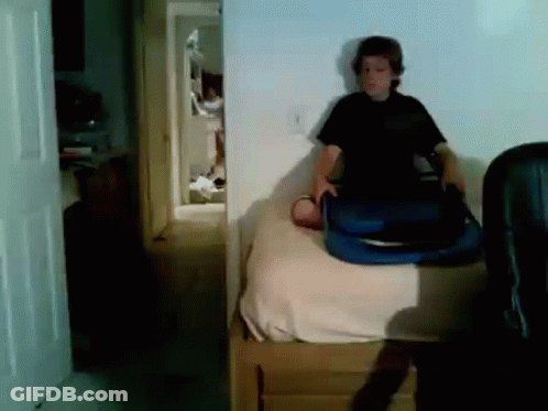 A Boy Is Sitting On A Bed Holding A Blue Suitcase GIF