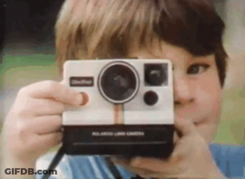 A Boy Is Taking A Picture With A Polaroid Land Camera GIF