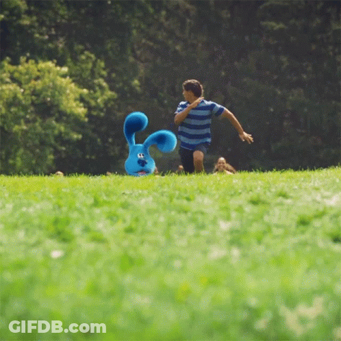 A Boy Runs Towards A Stuffed Blue Bunny In The Grass GIF