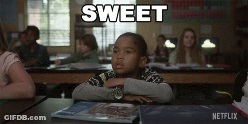 A Boy Sits At A Desk In A Classroom With The Word Sweet Written Above Him GIF