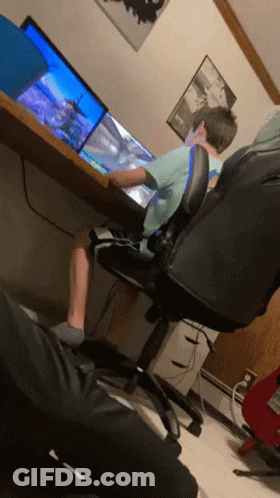 A Boy Sits At A Desk Playing A Video Game On A Computer GIF