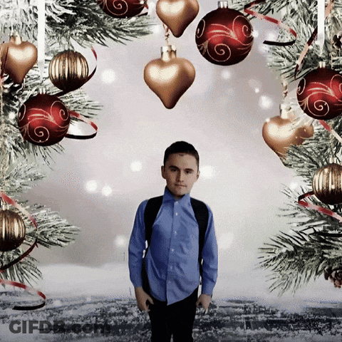 A Boy Stands In Front Of A Christmas Tree Surrounded By Decorations GIF