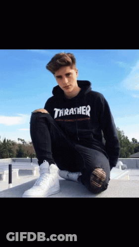 A Boy Wearing A Black Thrasher Hoodie Sits On A Ledge GIF