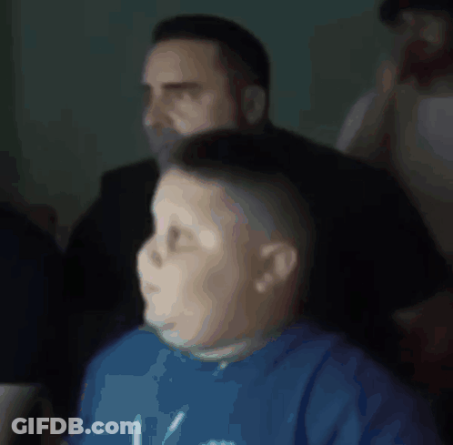 A Boy Wearing A Blue Shirt With The Letter V On It Is Sitting In Front Of A Man GIF