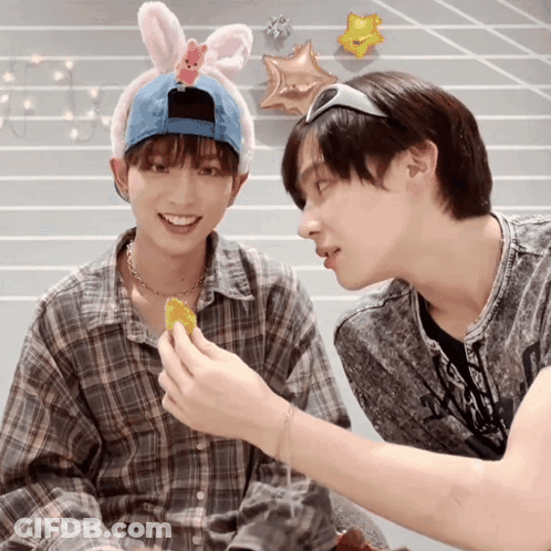 A Boy Wearing A Bunny Headband Is Feeding Another Boy A Snack GIF
