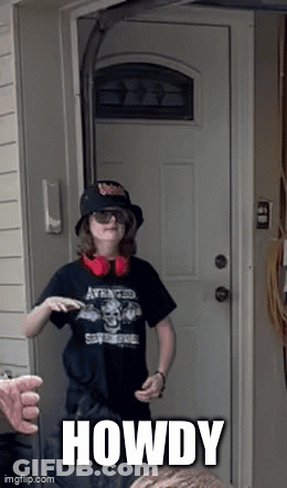 A Boy Wearing A Hat And Headphones Is Standing In Front Of A Door With The Word Howdy Written On It GIF
