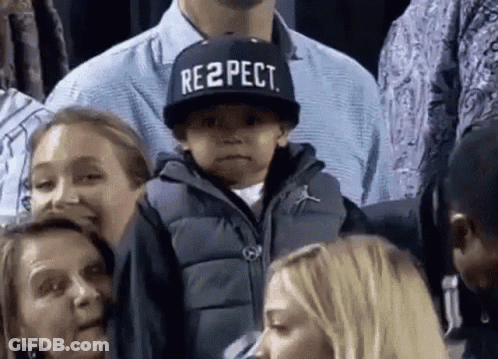 A Boy Wearing A Hat That Says Respect Is Sitting In A Crowd Of People . GIF