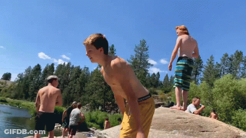 A Boy Wearing A Pair Of Converse Shorts Stands On A Rock Overlooking A River GIF